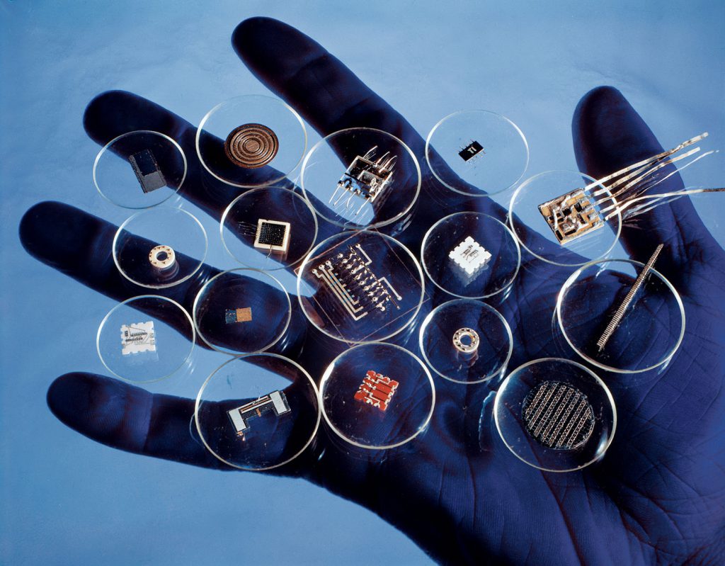 Goro photograph of early microcontrollers being held up in the palm of a hand in contrasting blue light.